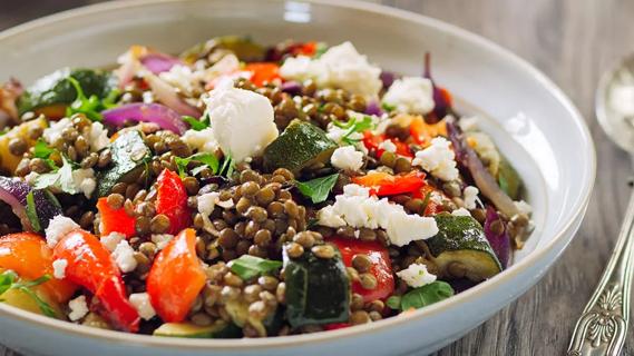 Closeup of a lentil salad containing lentils, cauliflower, peppers, zucchini in a white bowl on a wooden table