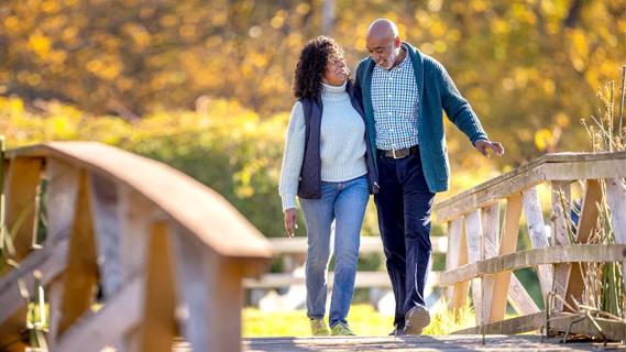 Older couple talk while leisurely walk across a bridge