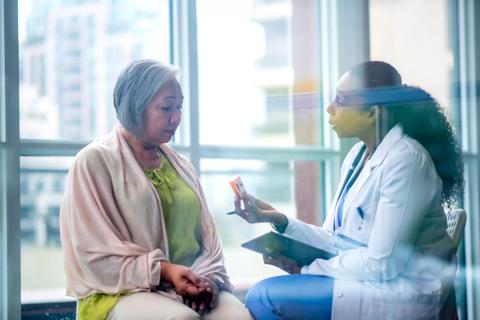 Healthcare provider holding prescription bottle talking with older female