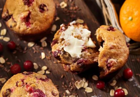 Close up of cranberry orange muffins with butter on half of muffin, set on wooden tray.