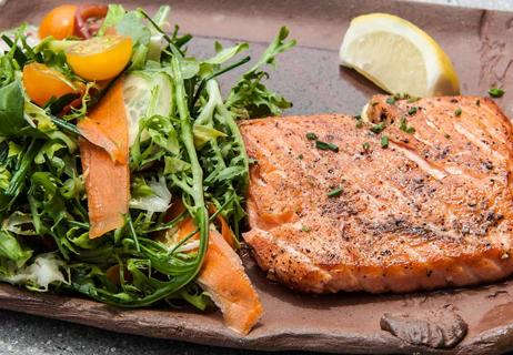 Baked salmon with a salad on the side plated on an individual clay platter.