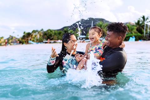 Caregivers holding toddler, playing in ocean