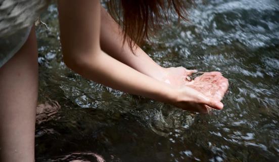 Person scooping up water in hands from creek