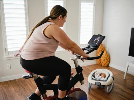 Female riding an exercise bike while newborn baby sleeps nearby