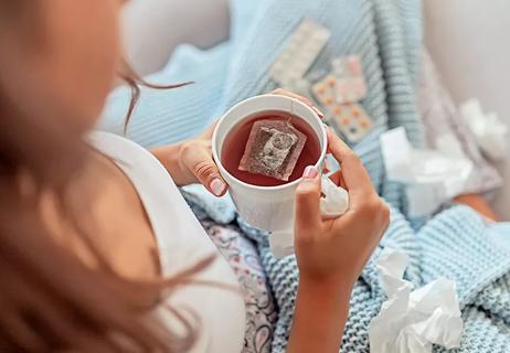 Overhead view of a person holding hot tea and flu medications.