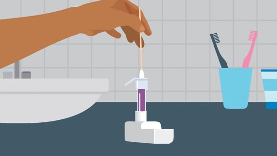 Hand holding nasal swab, pushing it into at-home COVID/flu test vial on counter in bathroom