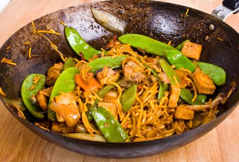 Tofu noodles, pea pods and tai peanut sauce in a wok skillet