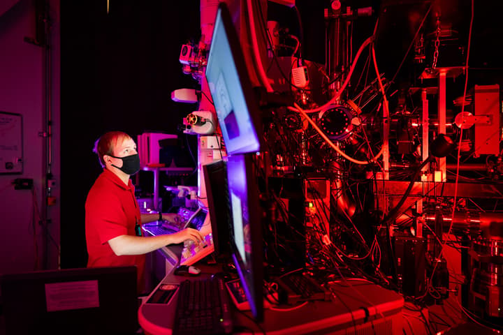 Researcher wearing face mask in a red-lit room looking at computer screens