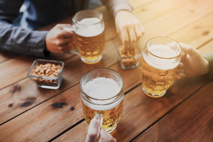 people, leisure and drinks concept - close up of male hands with beer mugs and peanuts at bar or pub