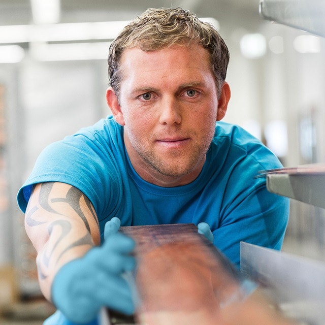 Person mit Schutzhandschuhen bei der Arbeit auf einer metallischen Oberfläche in einer Werkstattumgebung