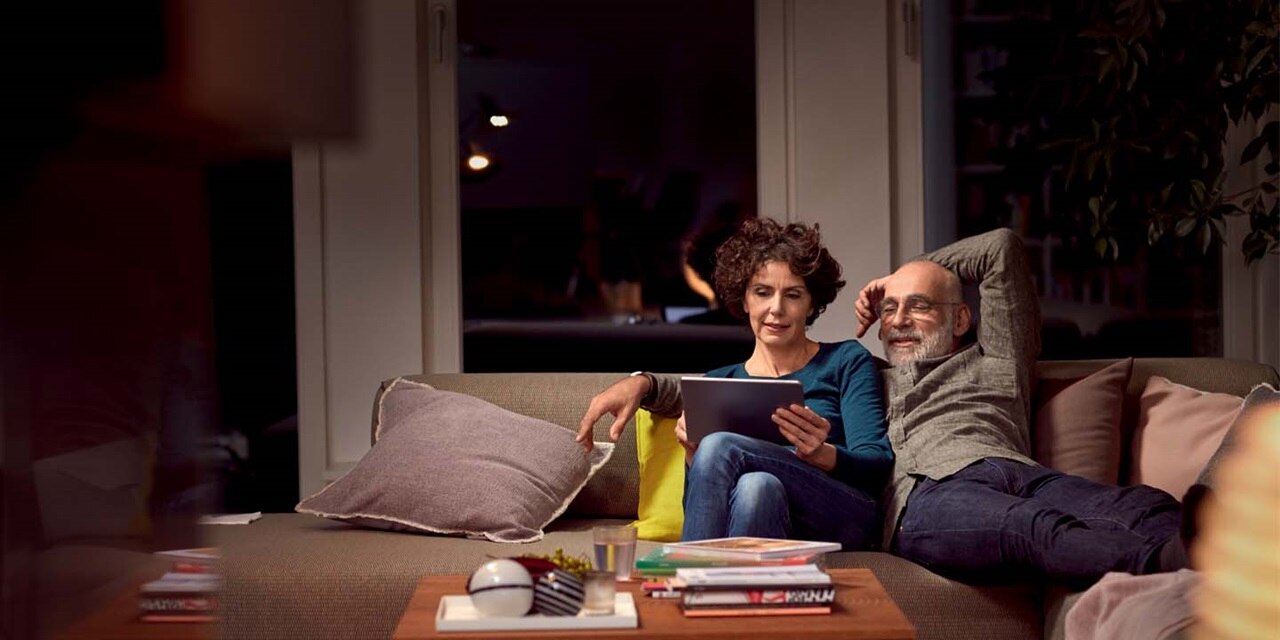 Deux personnes se détendant sur un canapé avec une tablette dans un salon cosy avec un éclairage doux
