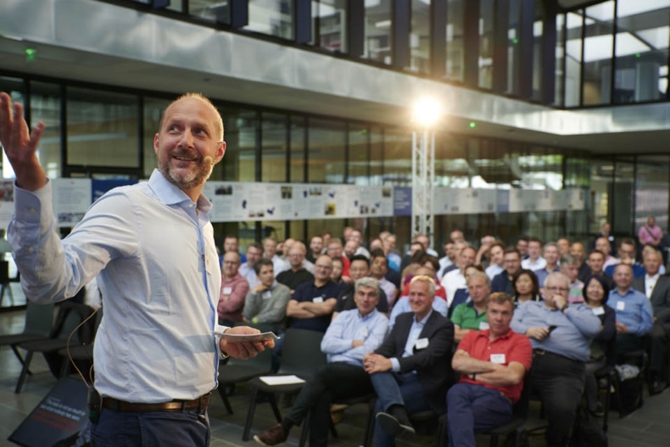 Présentateur interagissant avec l'audience lors d'une conférence dans un lieu moderne avec des luminaires suspendus visibles