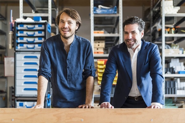 Dois funcionários sorrindo em um armazém industrial com componentes elétricos ao fundo