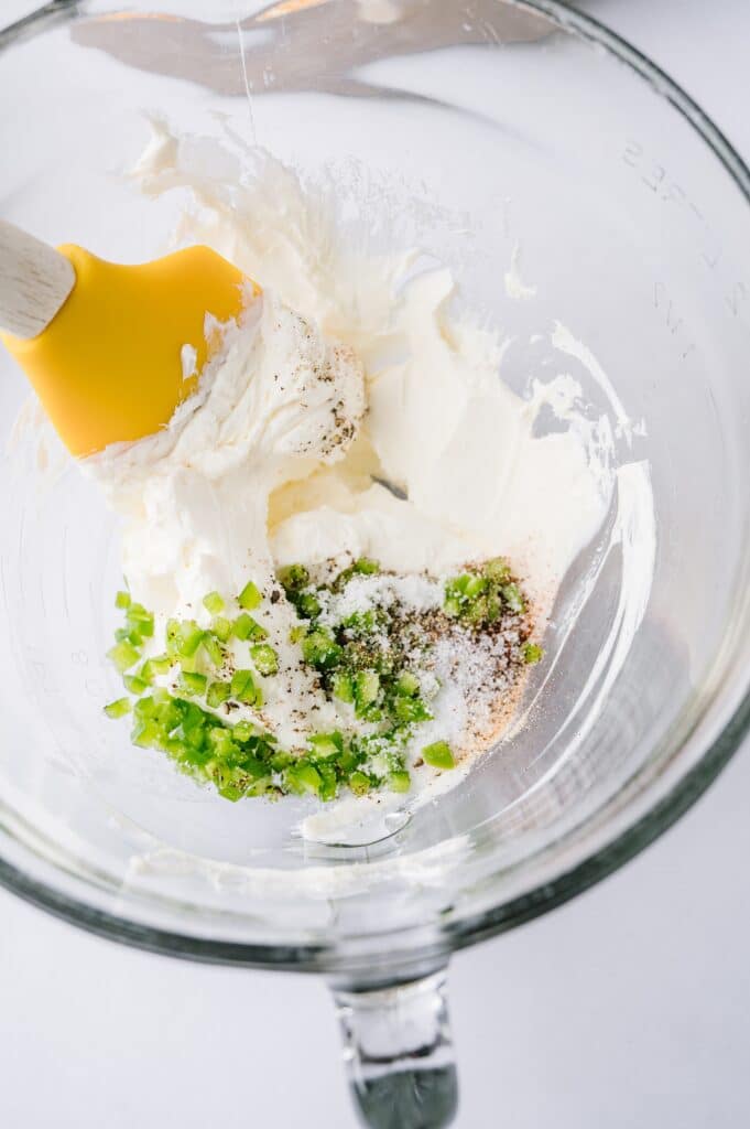 ingredients for hot corn dip being mixed in a bowl with a spatula