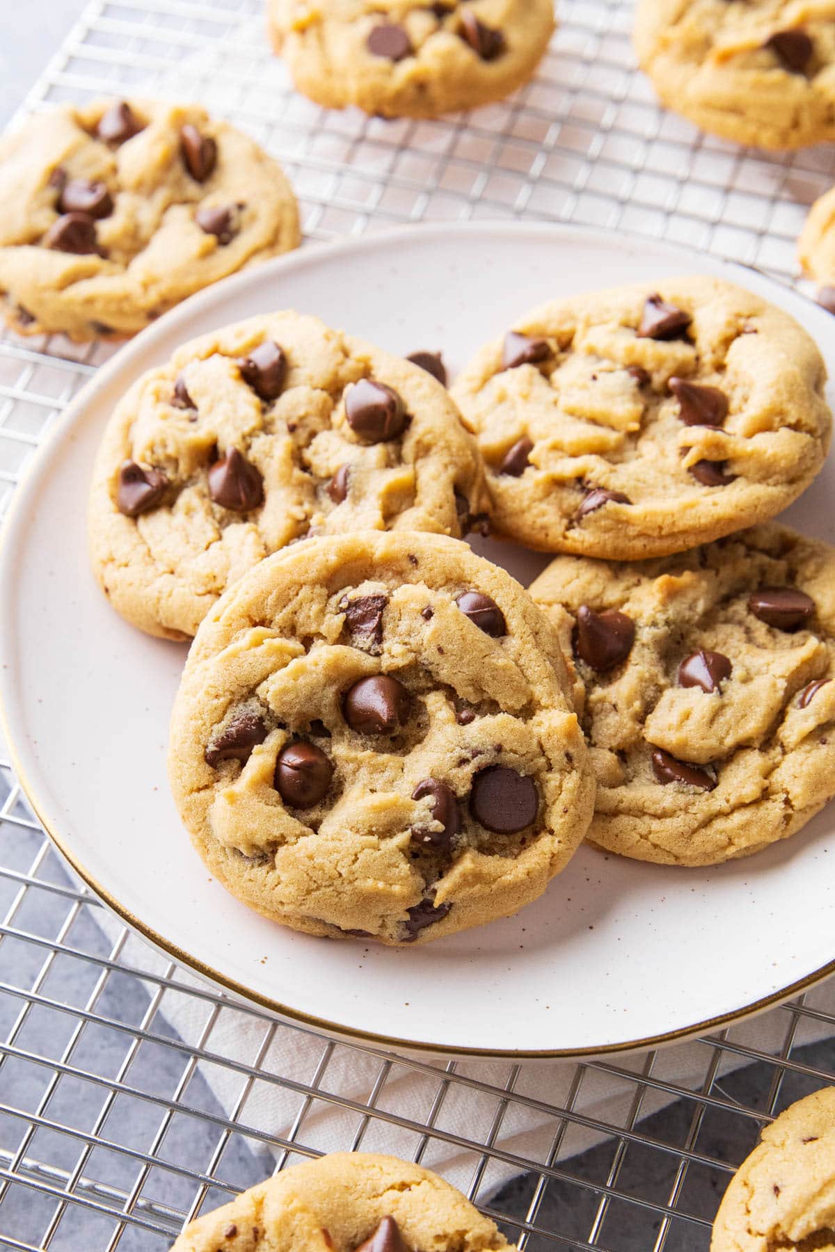 Four peanut butter chocolate chip cookies freshly baked, sitting on a plate surrounded by more crisp-edged, peanut butter-packed cookies.