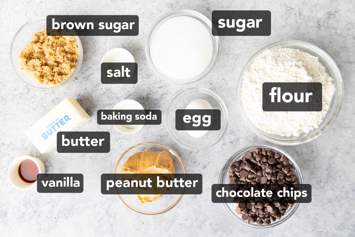 Ingredients for peanut butter chocolate chip cookies measured into prep bowls including peanut butter, chocolate chips, baking soda, flour, salt, vanilla, butter, granulated sugar, brown sugar, and room temperature egg.