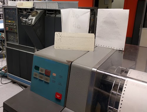 A greeting card with a tree and "Ho Ho Ho" inside, created on the vintage 1401 mainframe. The cards are on top of the 1403 line printer, and the 1401 mainframe is in the background.