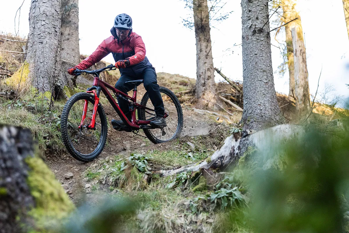 Male rider in orange and black top riding the Merida One-Forty 500 full suspension mountain bike in woodland