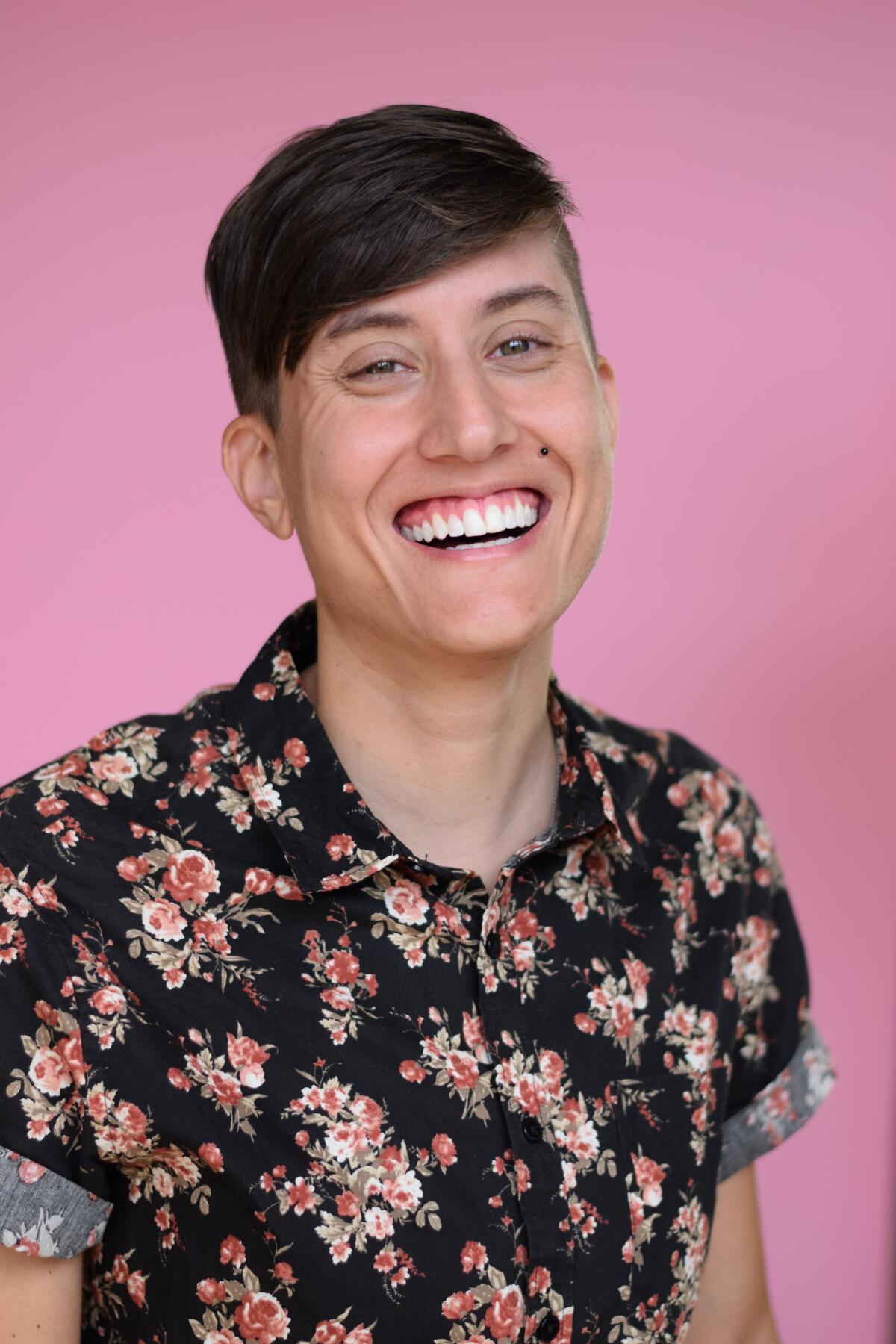 A headshot of a man wearing a floral short-sleeve button-down smiling