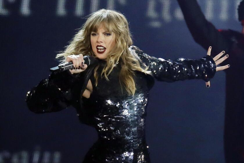 A woman in a shiny black outfit sings into a microphone while on stage