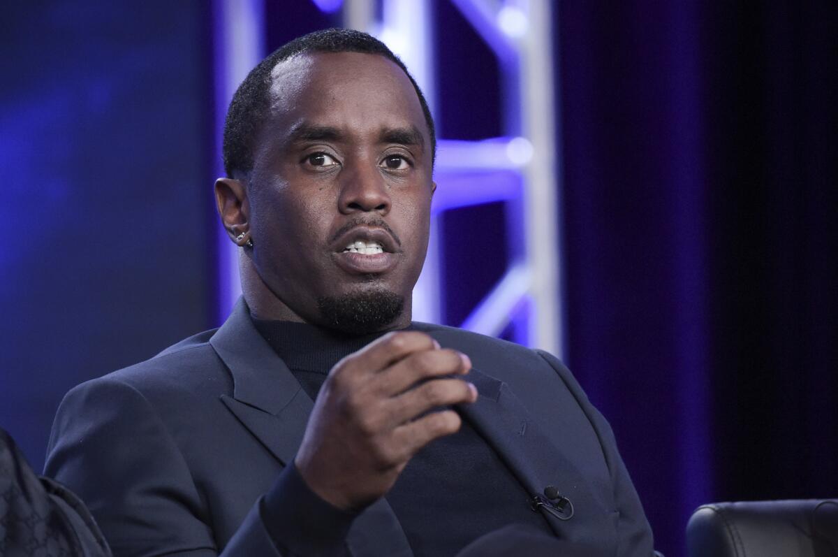 Sean 'Diddy' Combs is seated wearing a suit and motioning with his right hand