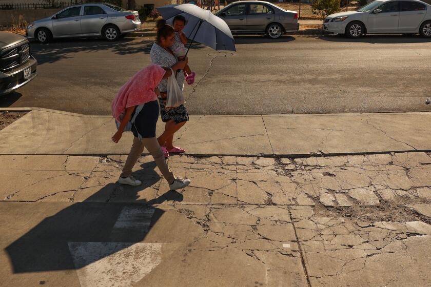 Pacoima, CA - September 06: A family walks by while holding an umbrella and covering their head with a shirt on Friday, Sept. 6, 2024 in Pacoima, CA. (Michael Blackshire / Los Angeles Times)