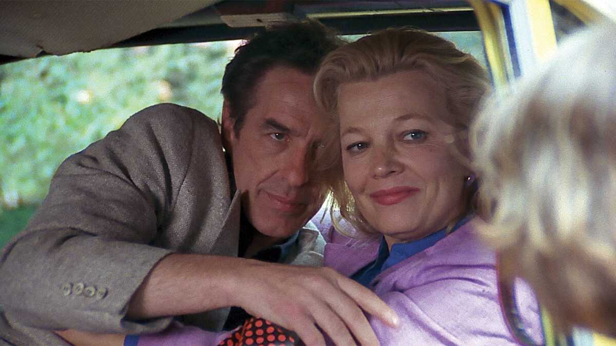 A woman and a man pose in a car.