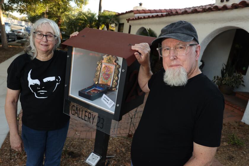 Long Beach, CA - September 07: Dave Clark and Carol Clark pose for a portrait in front of Ray Vasquez art piece which is showcased as little exhibitions in a box in the Wrigley neighborhood on Saturday, Sept. 7, 2024 in Long Beach, CA. (Michael Blackshire / Los Angeles Times)