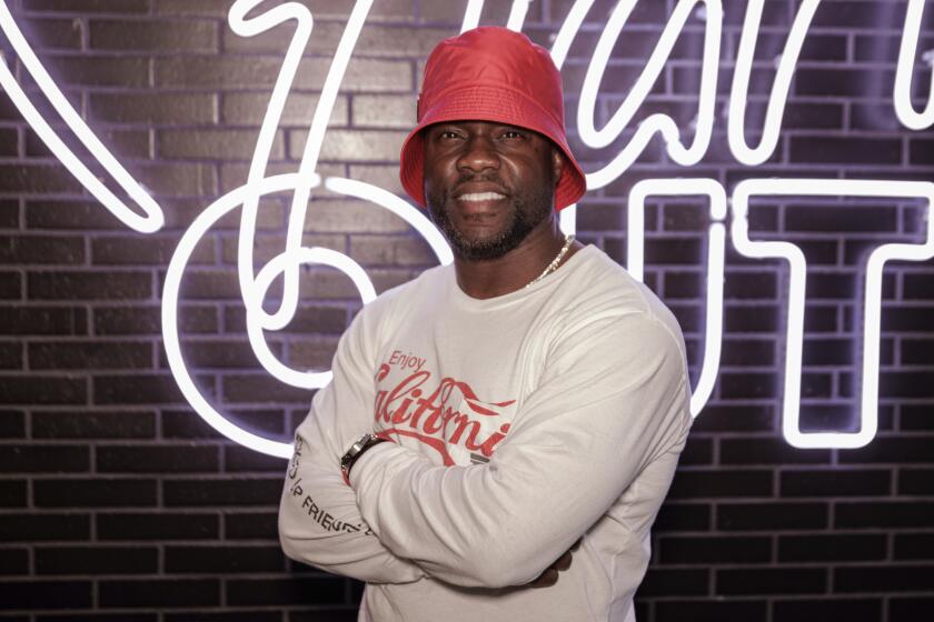 A man in a bucket hat smiles while posing with arms crossed in front of a tiled wall