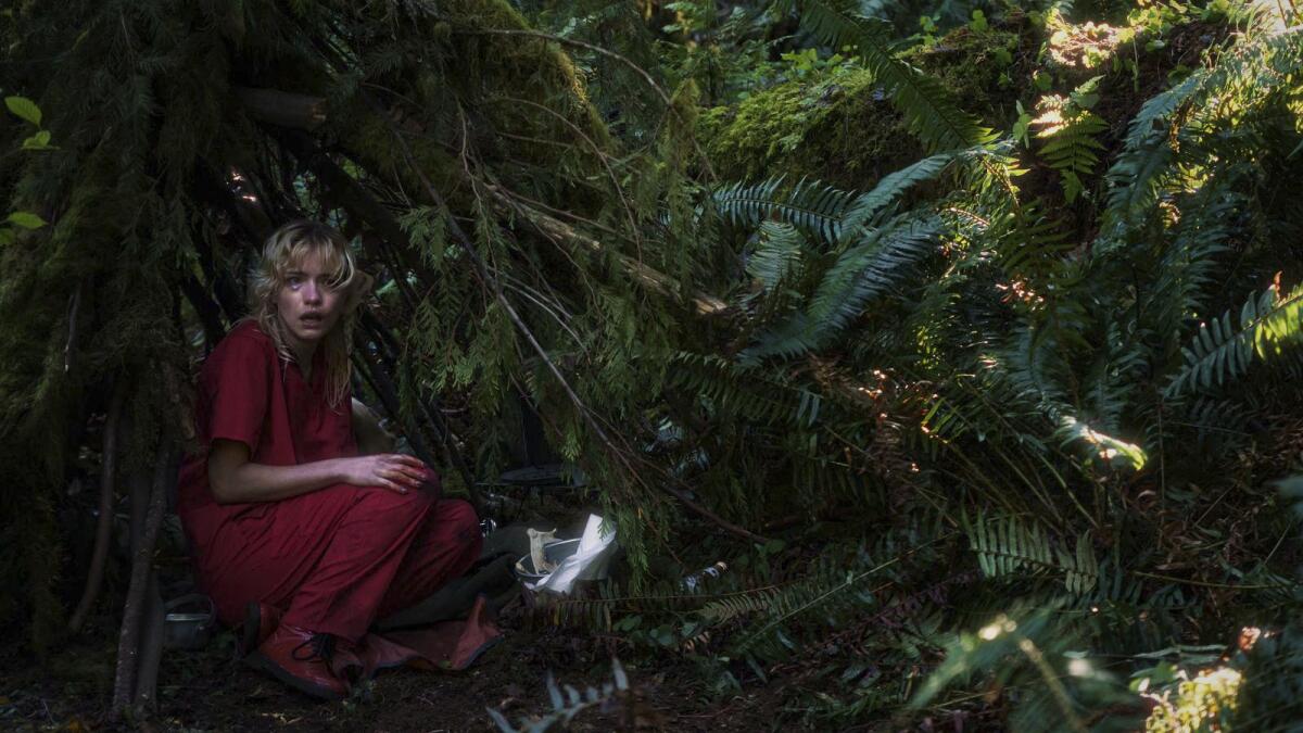 A woman in red crouches in a forest.