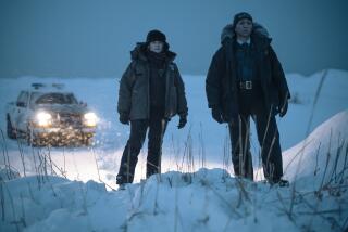 Two police officers standing on a snowdrift at night, illuminated by the headlights of their truck.