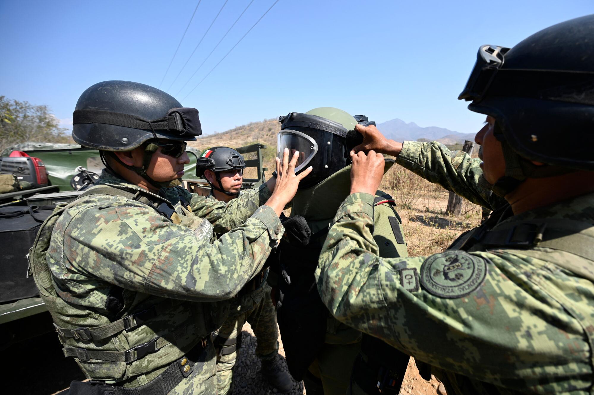 Soldiers help another soldier put on equipment 