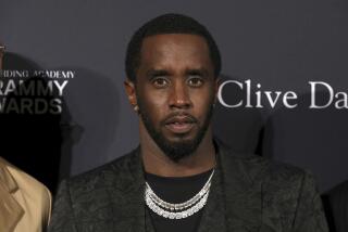 Sean "Diddy" Combs in a black blazer, black shirt and chains looking ahead as he poses at a red carpet