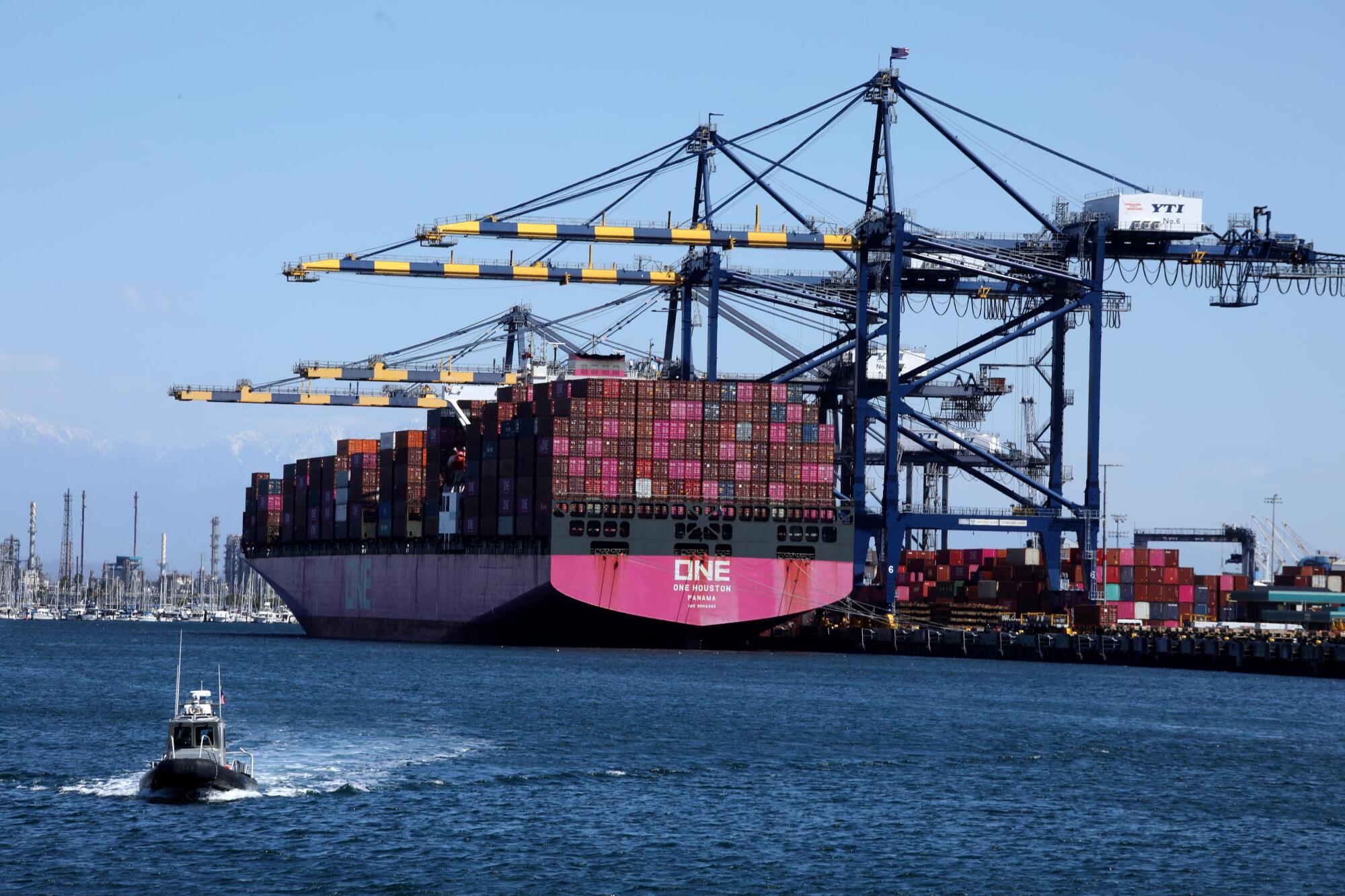 A tug boat makes its way through the Los Angeles Harbor against a backdrop of a ship laden with cargo containers.