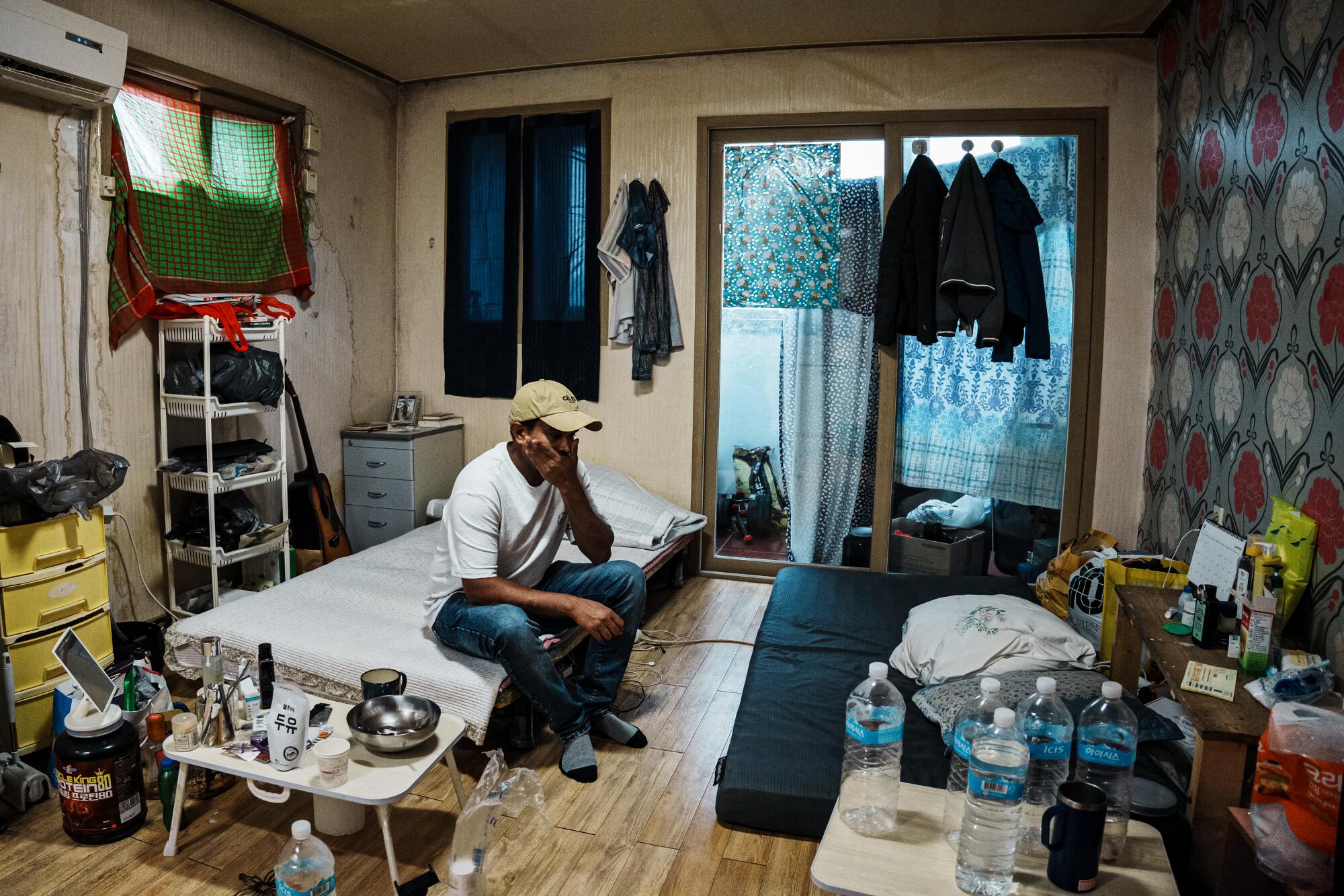 A man sitting on one of two beds in a cramped room