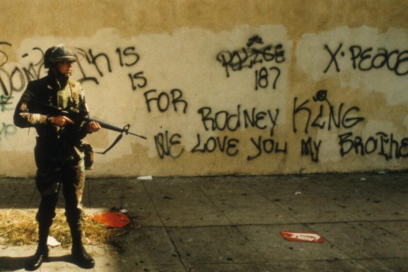 4–30–1992 National Guardsmean stands at alert near graffiti that spells out support for Rodney King.