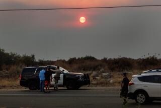 YUCAIPA, CA - SEPTEMBER 8, 2024: With the backdrop of a smoky sunset, a CHP officer advises residents at a road block on Highway 38 because of the Line fire on September 8, 2024 in Yucaipa, California. (Gina Ferazzi / Los Angeles Times)