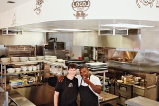 Daniel Patterson and Keith Corbin stand in the open kitchen of Locol in Watts. Corbin points at the camera.