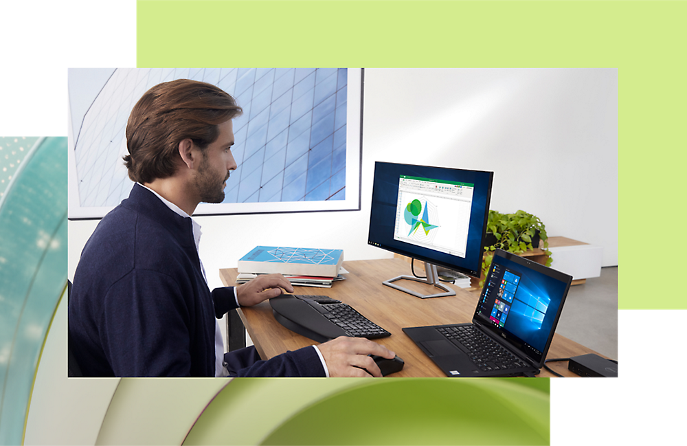 Hombre trabajando en un equipo de escritorio y portátil en un escritorio de oficina moderno, analizando datos en una pantalla con gráficos.