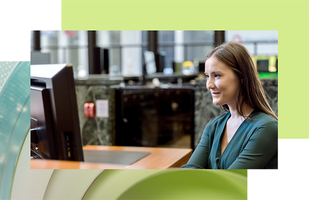 Una mujer con una parte superior verde sonríe mientras usa un equipo en una oficina.