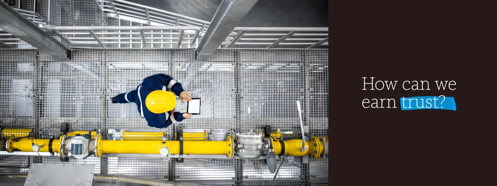 Aerial view of a person in a hardhat using a tablet in an industrial setting alongside the words “How can we earn trust?”