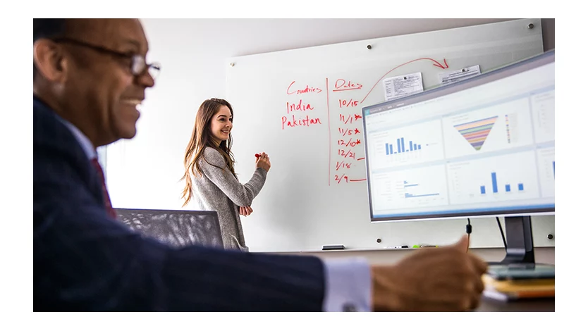 A woman writing on a whiteboard and collaborating with a man who is working on a computer