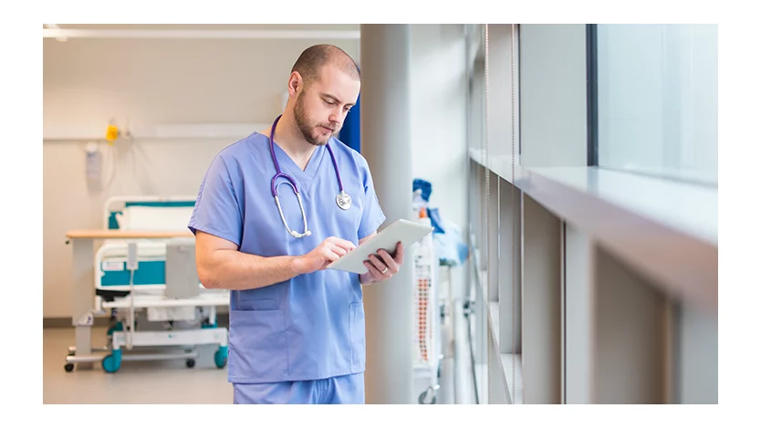 A doctor standing in a hospital wing reviewing a chart.