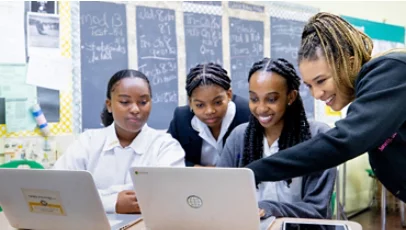 Young people in uniforms look at a laptop screen.