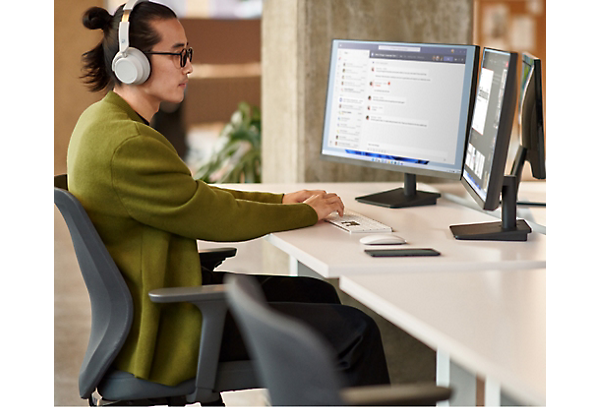 Una persona con auriculares y sentada en un escritorio con dos pantallas de ordenador