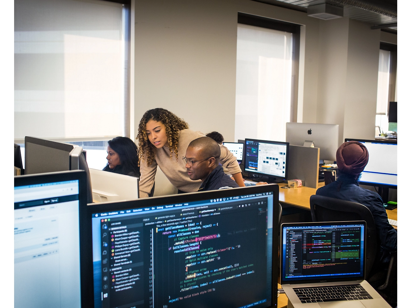 一群在办公环境中使用计算机的专业人士，注视着显示各种代码和数据的屏幕。