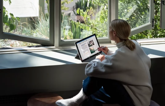 A person sitting in front of a large window using a 2 in 1 device.