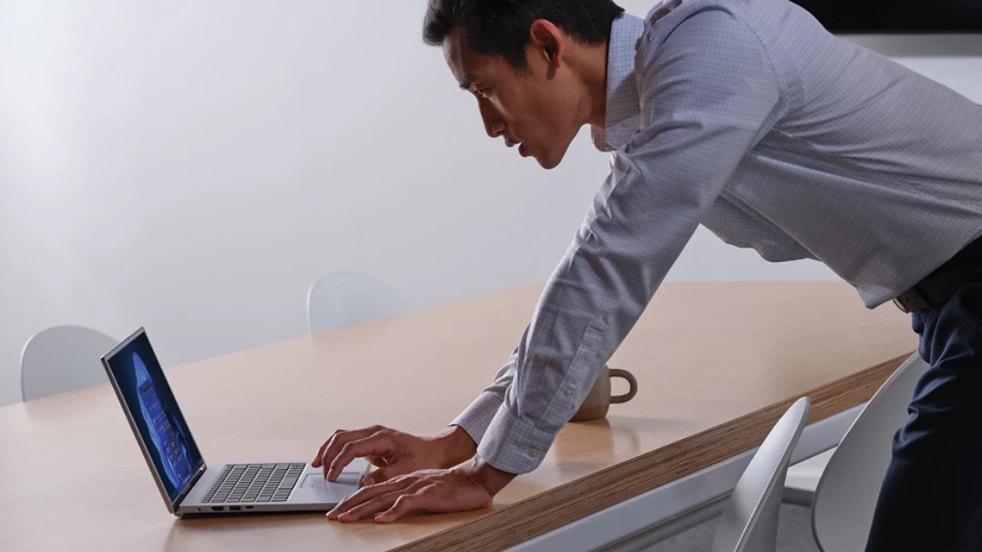 Un homme utilisant un ordinateur portable se penche au-dessus d’une table