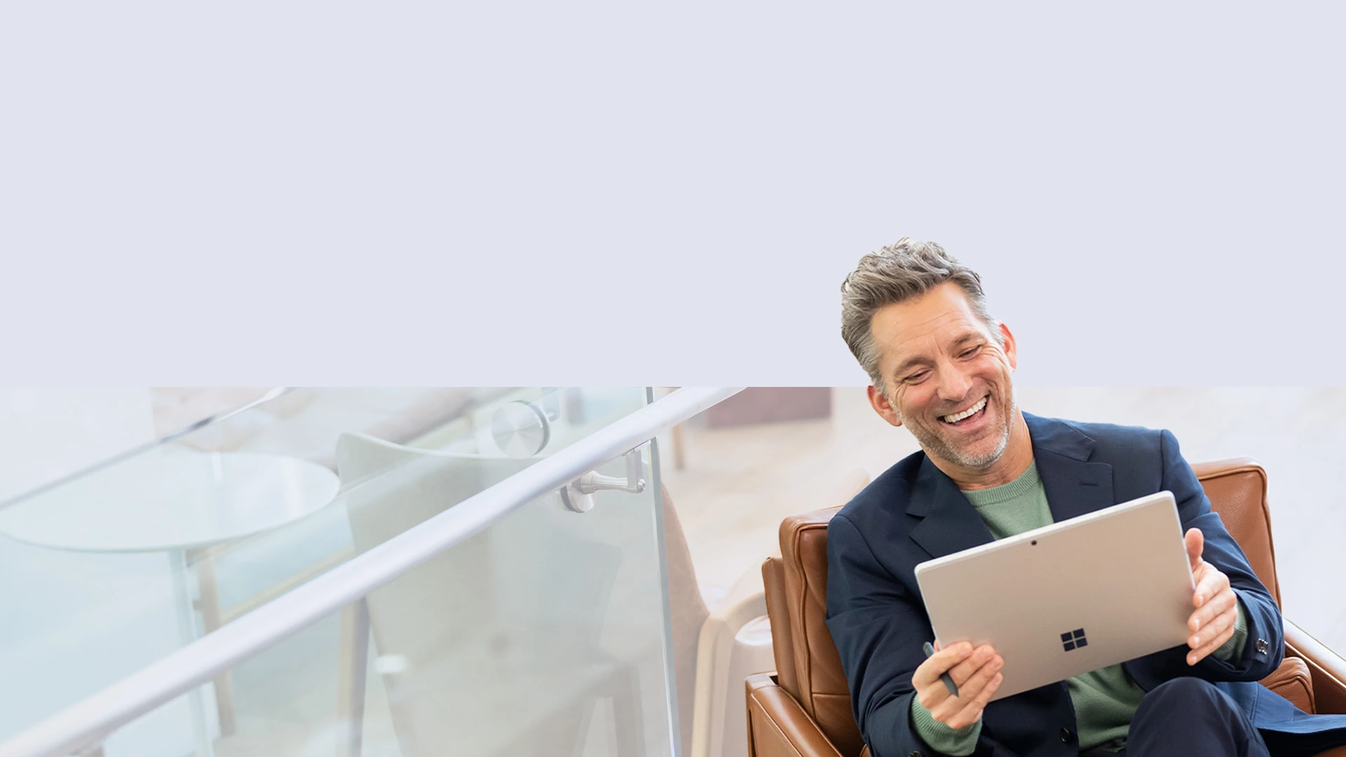 A man sitting on a couch holds a Surface Slim Pen 2 in his hand as he enjoys his Surface Pro 9