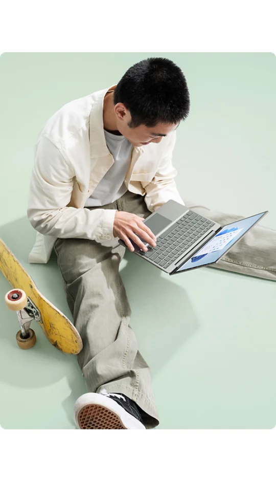 A young man takes a break from skateboarding to type a quick message on Surface Laptop Go 2.